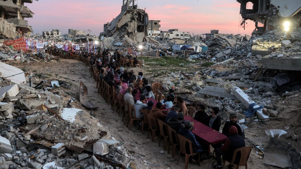 People gather among the rubble of destroyed buildings for a communal iftar fast-breaking meal on the second day of the Muslim holy month of Ramadan in in Gaza City's Tal al-Hawa district
