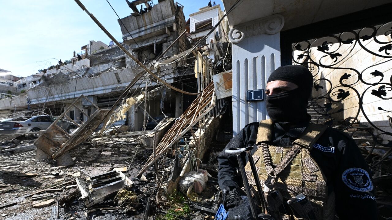 A member of the new Syrian administration's security forces stands guard at the site of an Israeli strike in a Damascus area where, a war monitor said, Palestinian leaders are known to reside