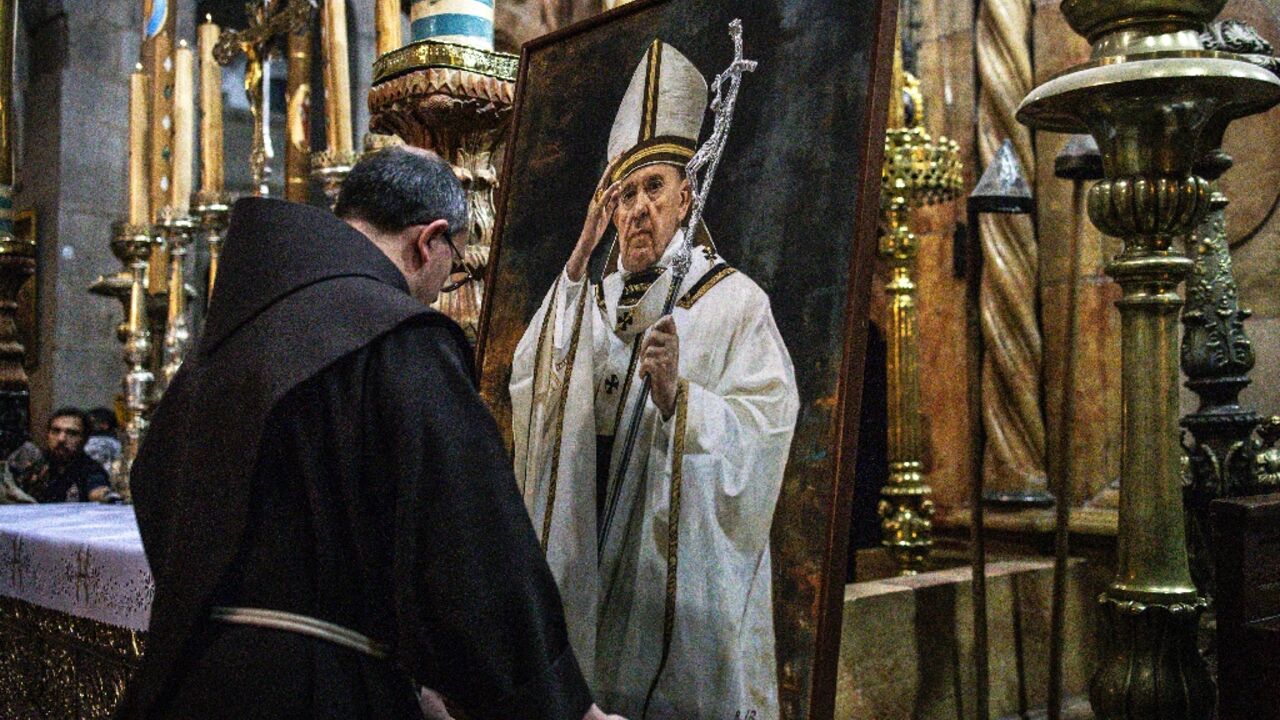 A Christian clergy man stands by a portrait of the late Pope Francis on a easel ahead of a memorial mass at the Church of the Holy Sepulchre 