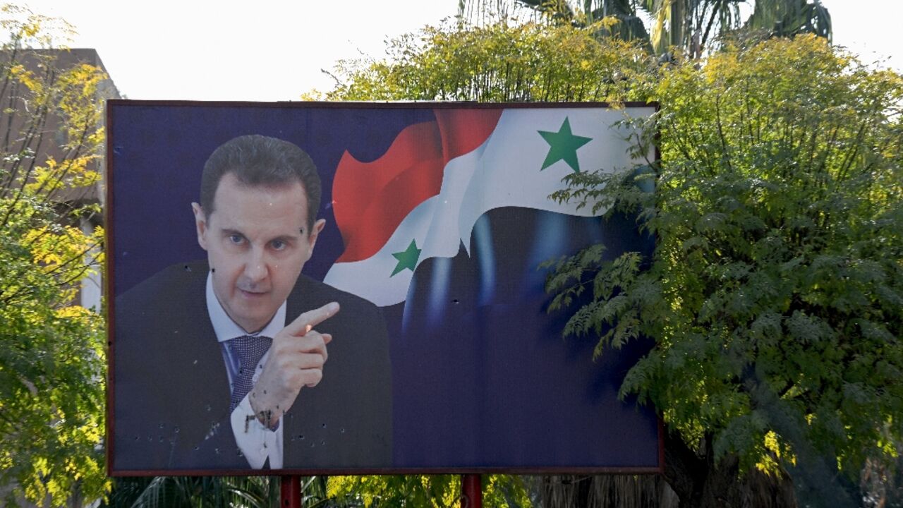 A portrait of ousted Syrian president Bashar al-Assad next to a national flag is slightly damaged by shrapnel outside the Barzeh scientific research centre north of the Syrian capital Damascus, after being targeted by a December 2024 Israeli airstrike