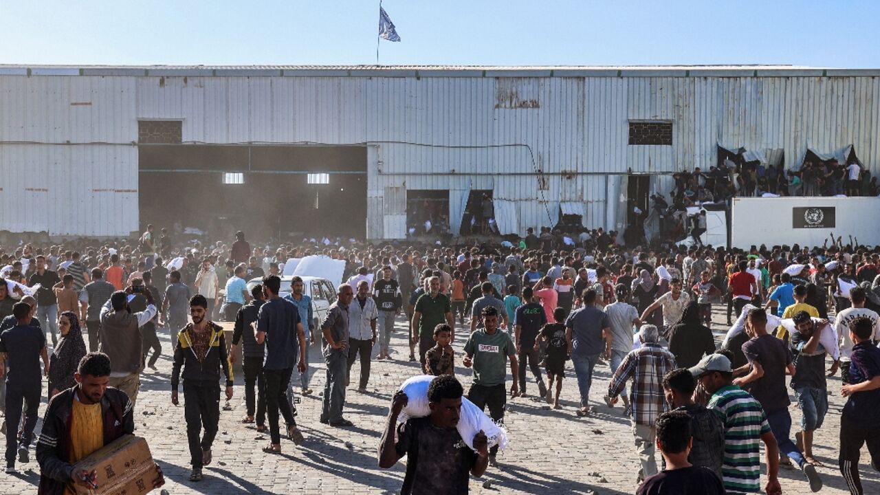 Displaced Palestinians ferry bags of food aid after storming a World Food Programme warehouse in Deir el-Balah in the central Gaza Strip on May 28, 2025