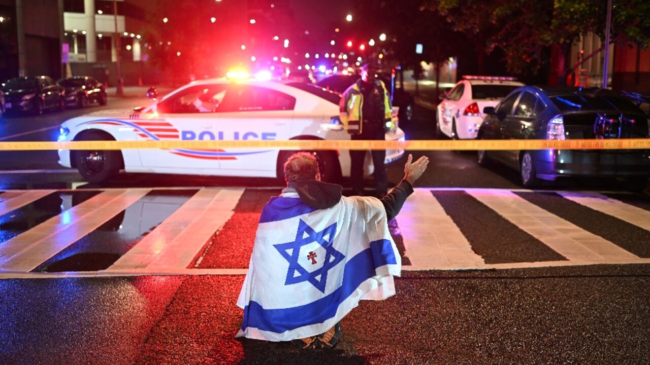 A man draped in the Israeli flag, bearing a cross and the name "Jesus" at its center, gestures as police secure the area outside the Capital Jewish Museum following a shooting that left two people dead in Washington, DC
