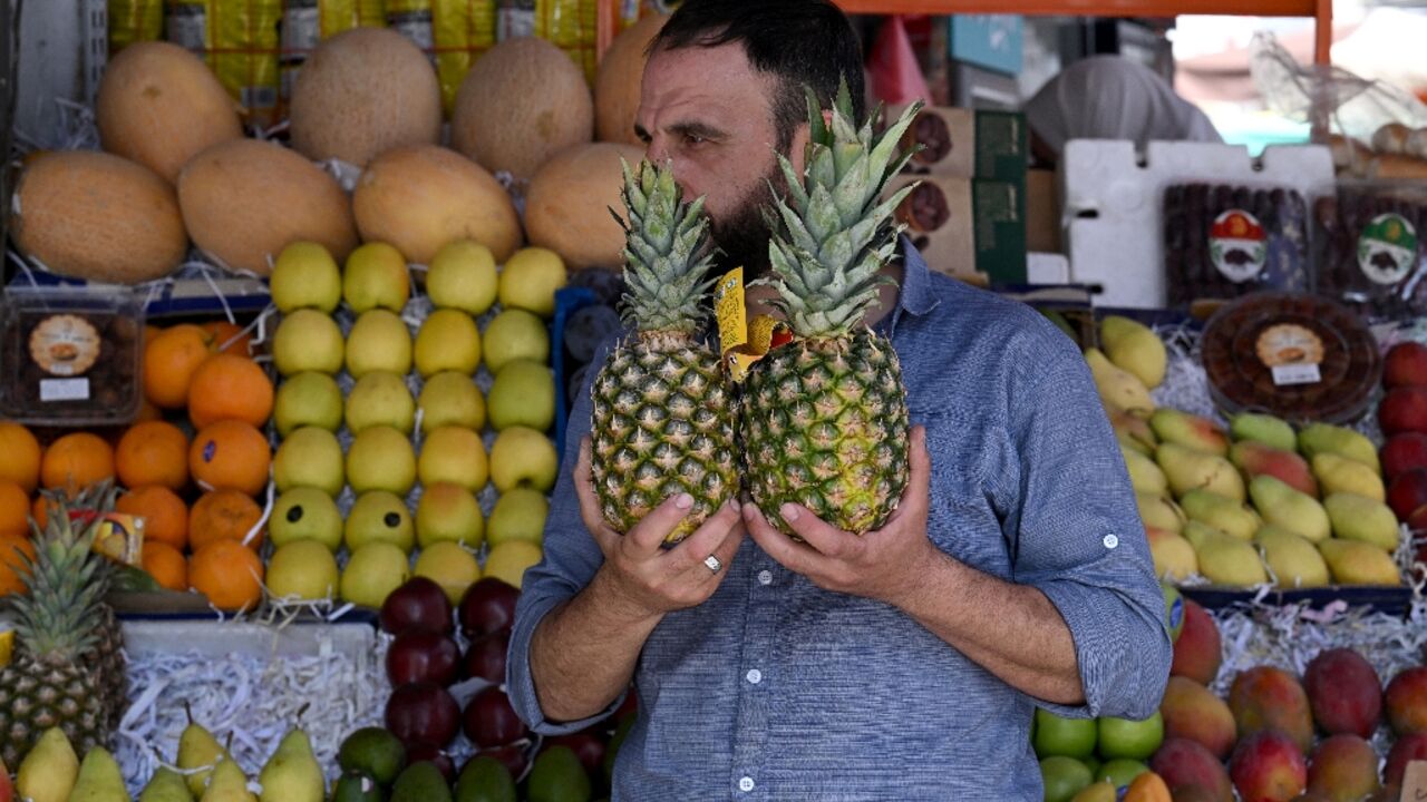 A man holds two pineapples at a stall selling fruits, many of which were not available while deposed president Bashar al-Assad was in power