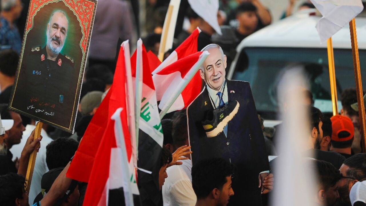 An Iraqi holds a picture of Major General Hossein Salami, head of the Iranian Revolutionary Guard, who was killed in an Israeli airstrike in Tehran, with another holding a cutout of Israeli Prime Minister Benjamin Netanyahu with a shoe around the neck during a protest in Baghdad