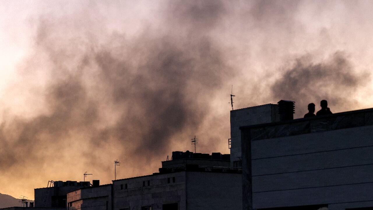 People stand on a rooftop as smoke wafts over Tehran following an Israeli strike