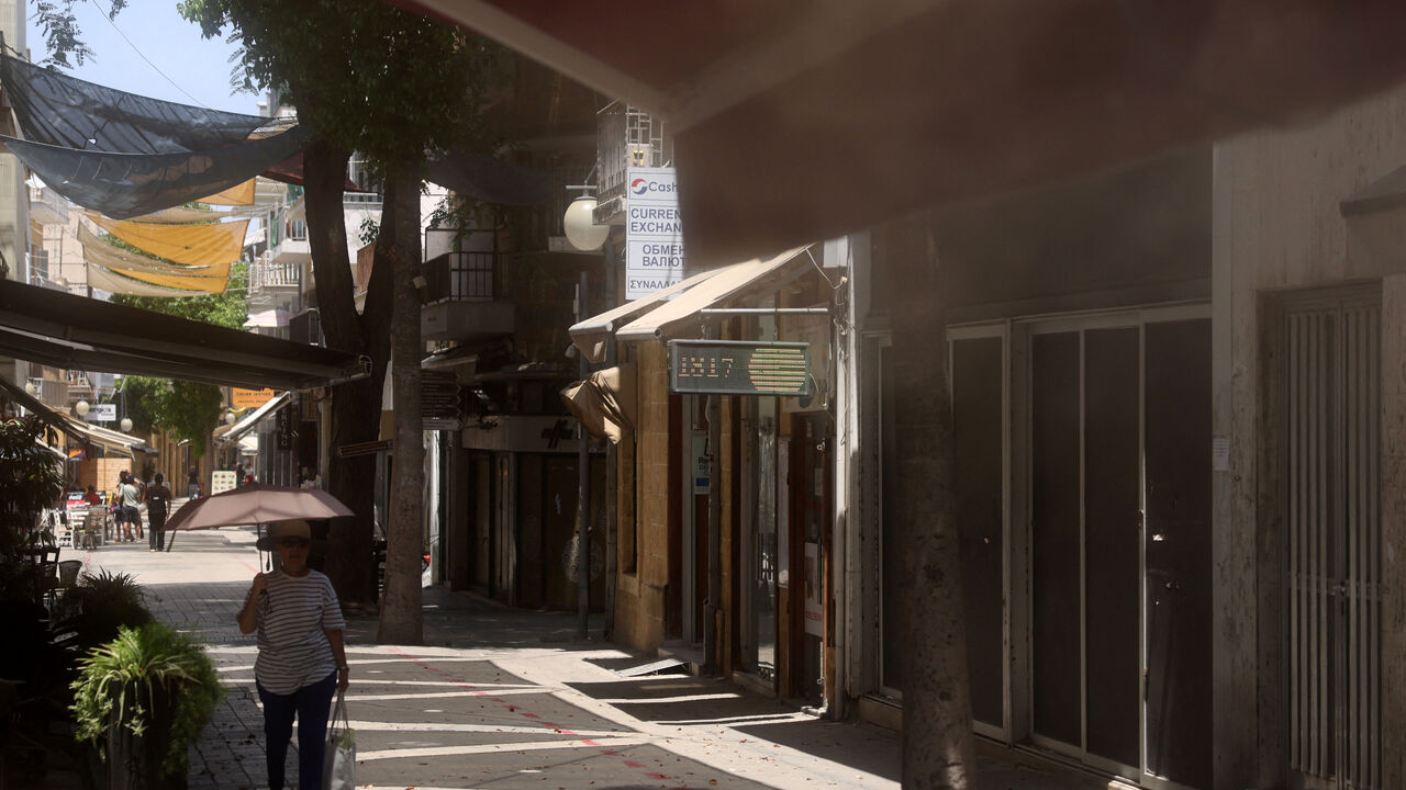 A woman shelters from the sun with an umbrella while a mist machine works at a coffeshop during a heatwave in Nicosia, Cyprus July  23, 2025. REUTERS/Yiannis Kourtoglou