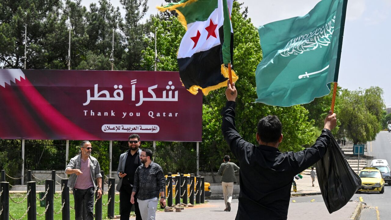A man carries the Syrian and the Saudi flags past a billboard thanking Qatar, in Damascus, on May 14, 2025. 
