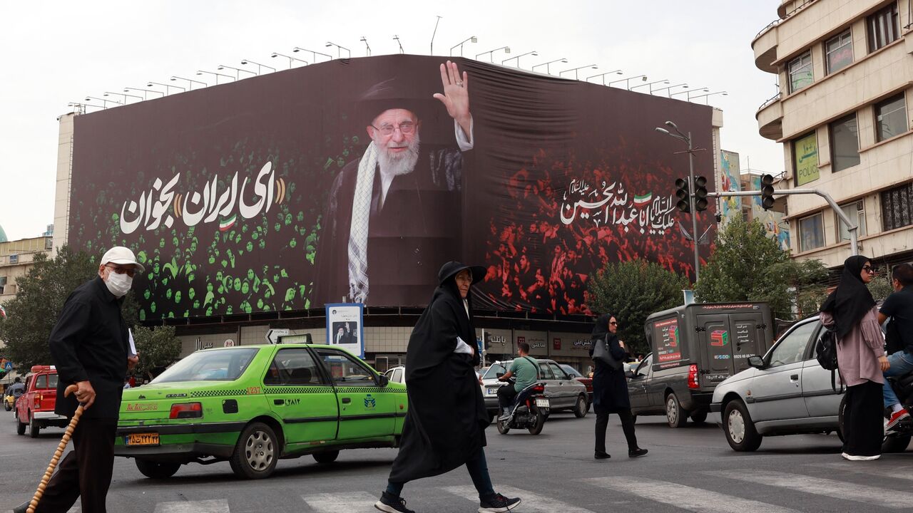 Iranians cross a street by a billboard with a portrait of Supreme Leader Ayatollah Ali Khamenei, Enqelab Square, Tehran, July, 9, 2025.