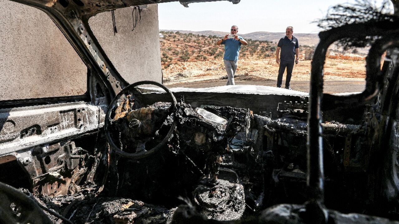 Men stand near a vehicle that was reportedly torched by Israeli settlers during an overnight attack on the Palestinian Christian village of Taybeh