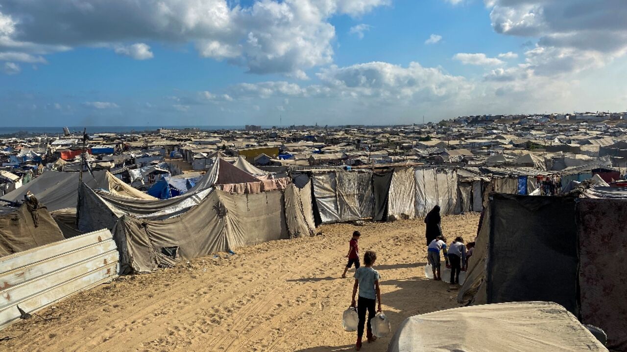 Palestinian children carry water past line after line of tents housing displaced families in the sand dunes of Mawasi on Gaza's Mediterranean coast.