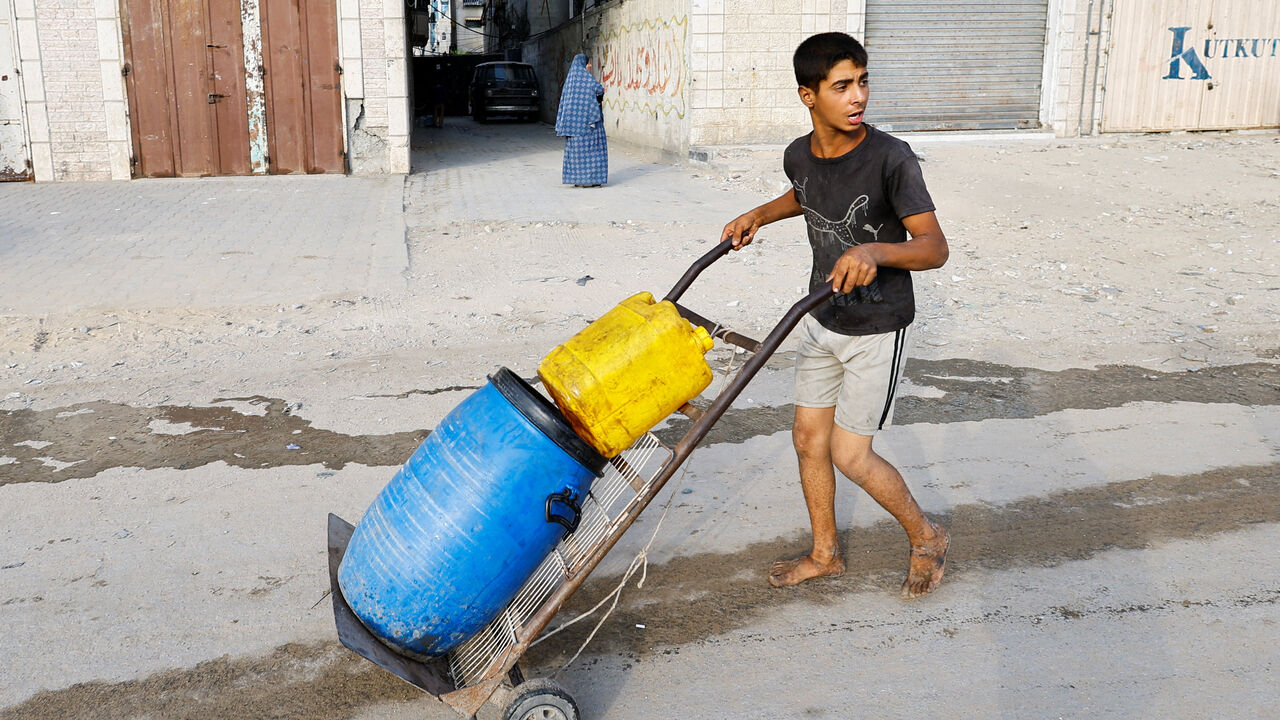 A boy pushes a trolley with containers as Palestinians wait to collect water amid shortages, in Gaza City August 6, 2025. REUTERS/Mahmoud Issa