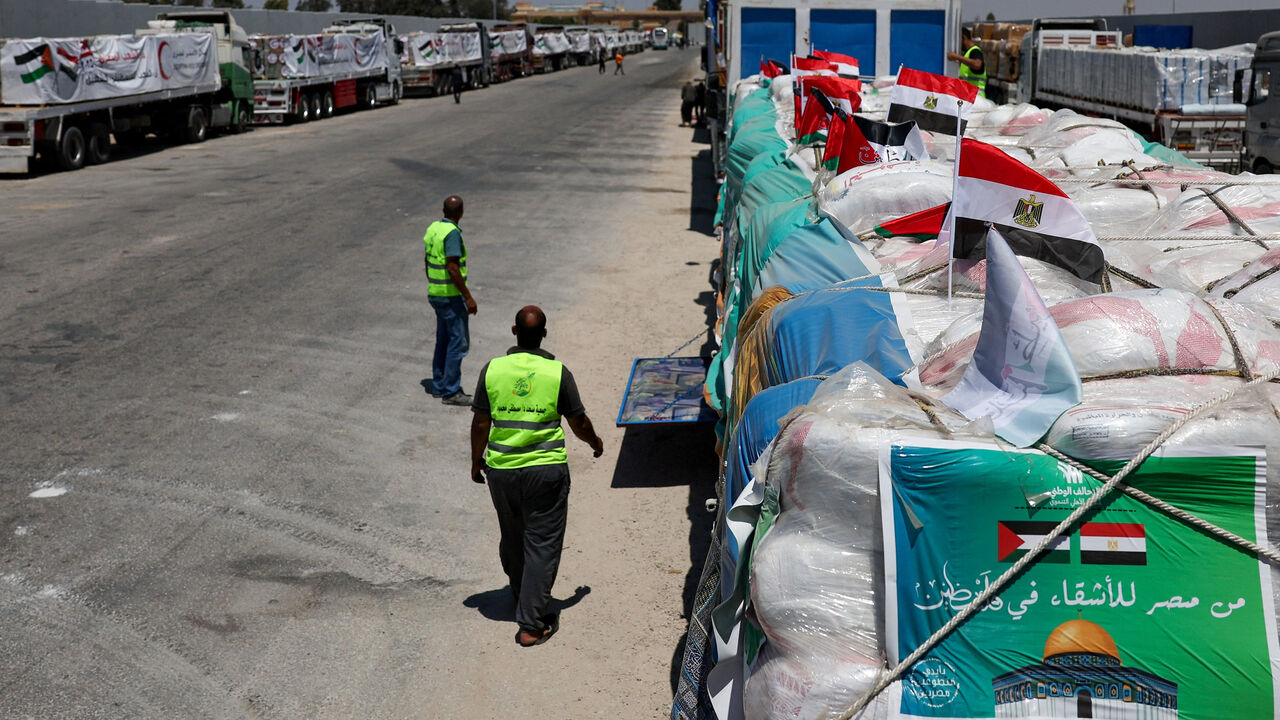 People walk next to trucks carrying humanitarian aid near the Rafah border crossing between Egypt and the Gaza Strip, in Rafah, Egypt, August 6, 2025. REUTERS/Amr Abdallah Dalsh