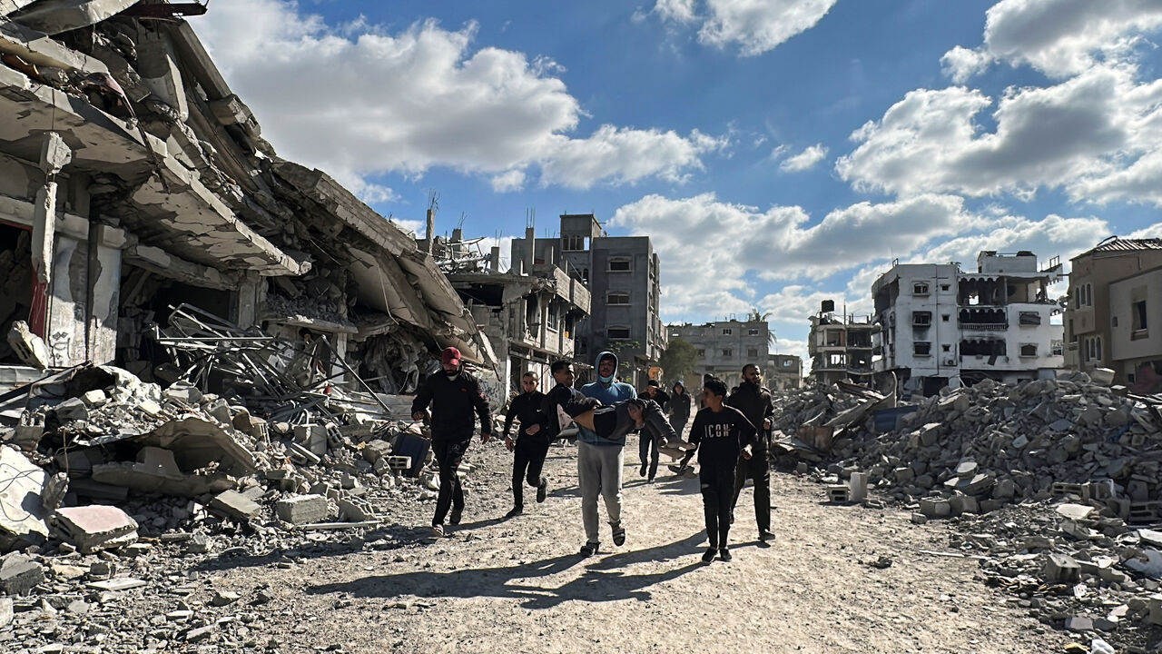 A man carries a wounded Palestinian as people walk past the rubble of houses and buildings destroyed during the war, following a ceasefire between Israel and Hamas, in Al-Bureij in the central Gaza Strip January 20, 2025. REUTERS/Khamis Saeed/File Photo