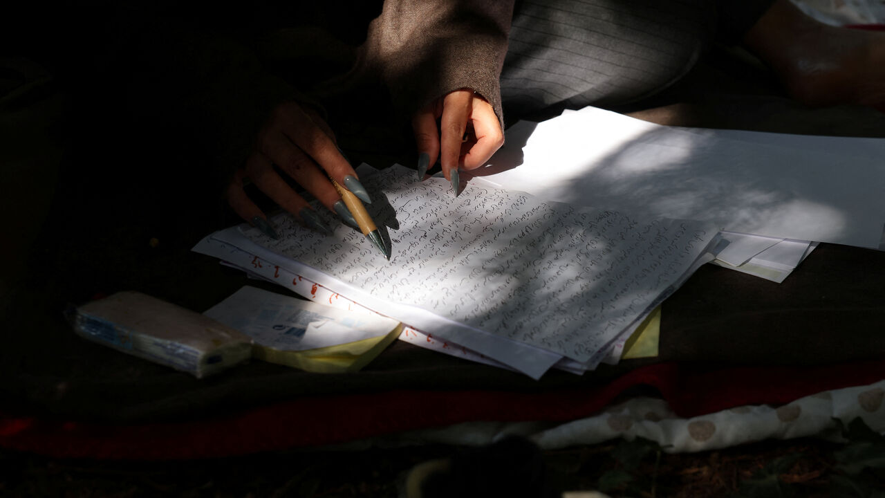 Nadia Feyzi, 32, an Afghan artist who fled conflict in her country and migrated to Germany, rereads a page of her manuscript that she has just finished writing while sitting in a cemetery that she goes to for inspiration in Bonn, Germany, July 15, 2025. Feyzi's book is inspired by the lives of Afghan women over generations and says, "I want to do something big here. This book will say it all.” REUTERS/Zohra Bensemra