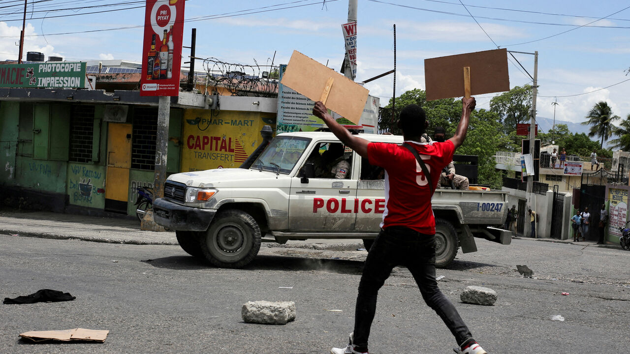 FILE PHOTO: A man holds up placards as he yells toward a patrol car during a protest against gang-related violence and to demand the resignation of Haiti's transitional presidential council, in Port-au-Prince, Haiti, May 15, 2025. REUTERS/Jean Feguens Regala/File Photo