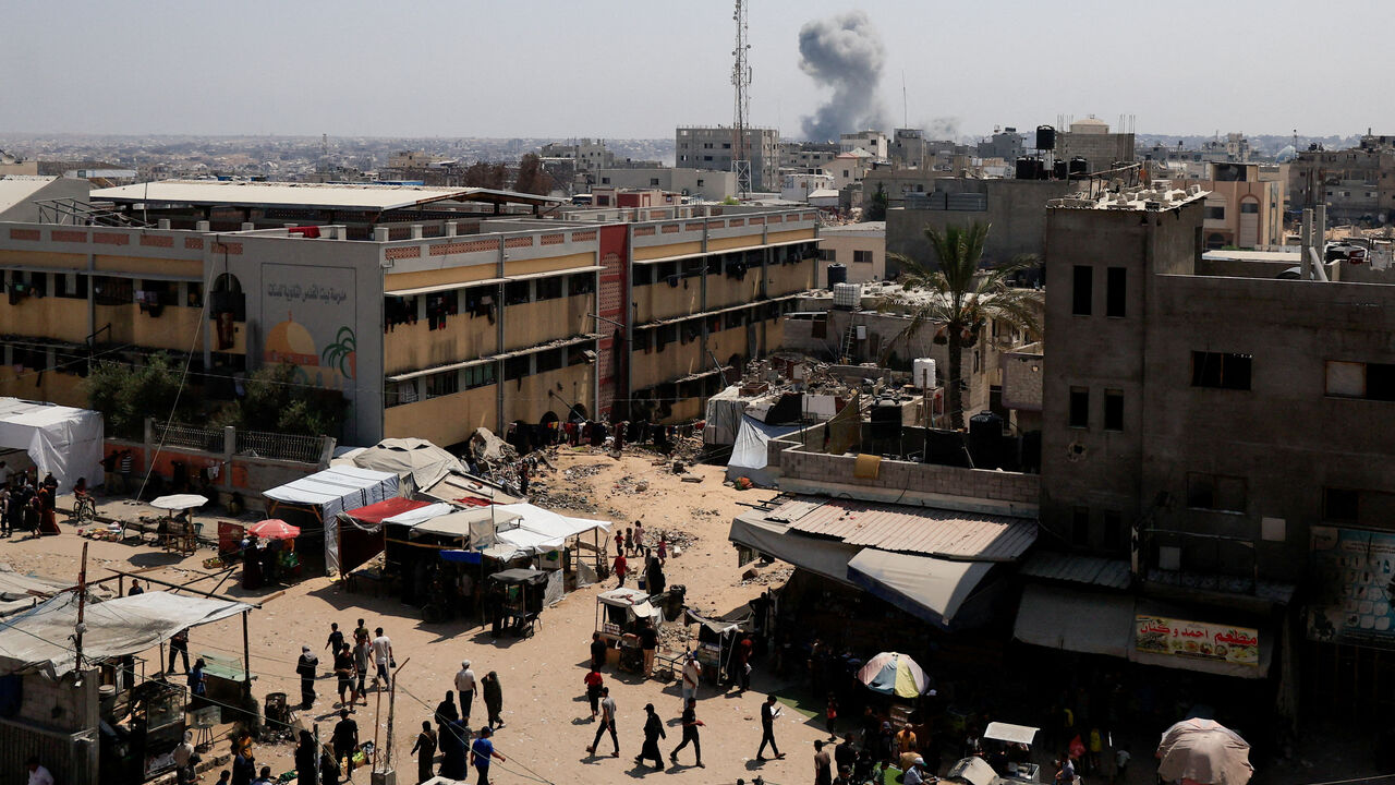 FILE PHOTO: Palestinians walk as smoke rises in the distance, following an Israeli strike, in Khan Younis in the southern Gaza Strip, August 14, 2025. REUTERS/Hatem Khaled/File Photo