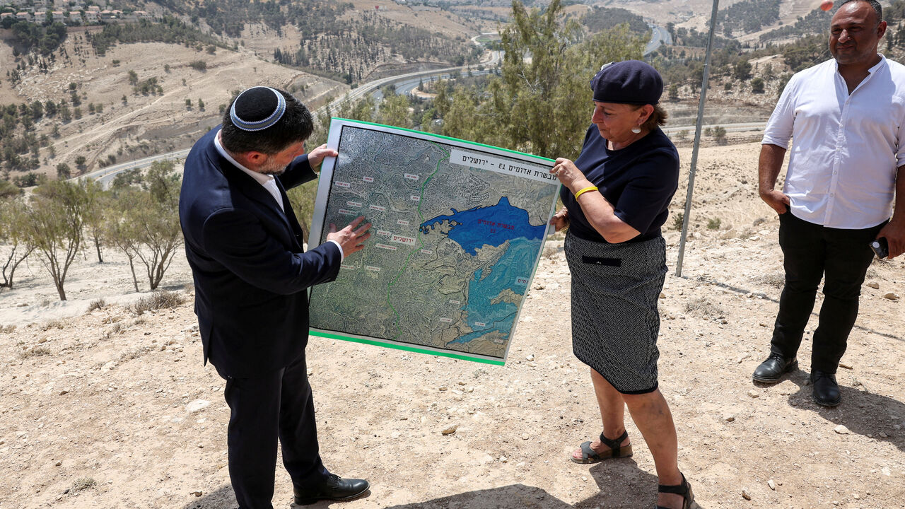 FILE PHOTO: Israeli Finance Minister Bezalel Smotrich and a woman hold a map that shows the long-frozen E1 settlement scheme, that would split East Jerusalem from the occupied West Bank, on the day of a press conference near the Israeli settlement of Maale Adumim, in the Israeli-occupied West Bank, August 14, 2025. REUTERS/Ronen Zvulun/File Photo