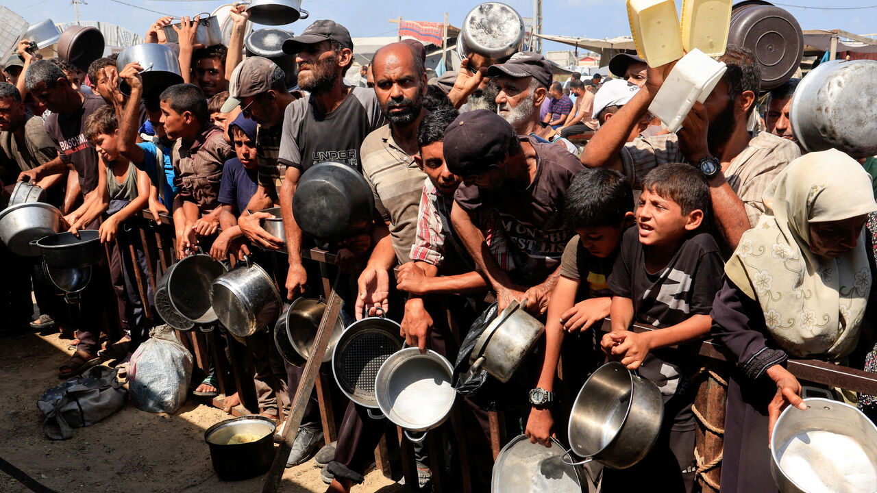FILE PHOTO: Palestinians hold pots and containers while waiting to receive food from a charity kitchen in Khan Younis, southern Gaza Strip, August 21, 2025. REUTERS/Hatem Khaled/File Photo