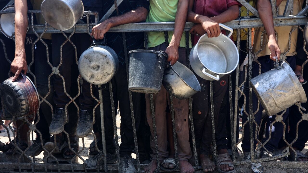 Palestinians carry empty pots as they wait to receive lentil soup at a food distribution point in Gaza City on August 2, 2025

