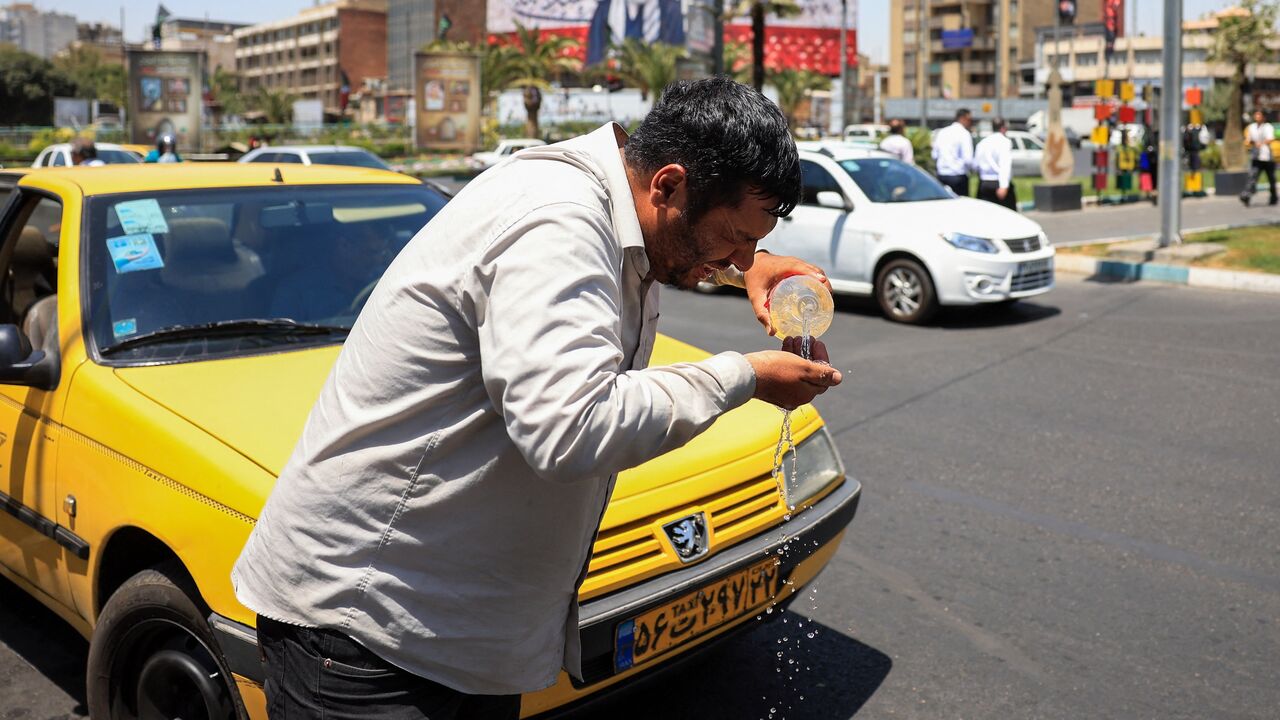 An Iranian taxi driver cools down by splashing water on his face on a street amid soaring temperatures in Tehran on July 22, 2025. 