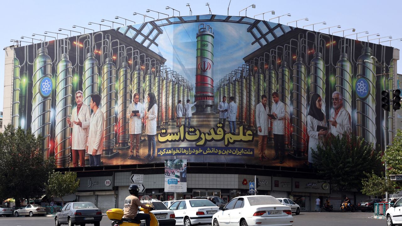Iranians drive next to a billboard displaying pictures of nuclear scientists, centrifuges and a sentence reading in Farsi " Science is the power," at the Enqelab Square in Tehran, on Aug. 29, 2025.