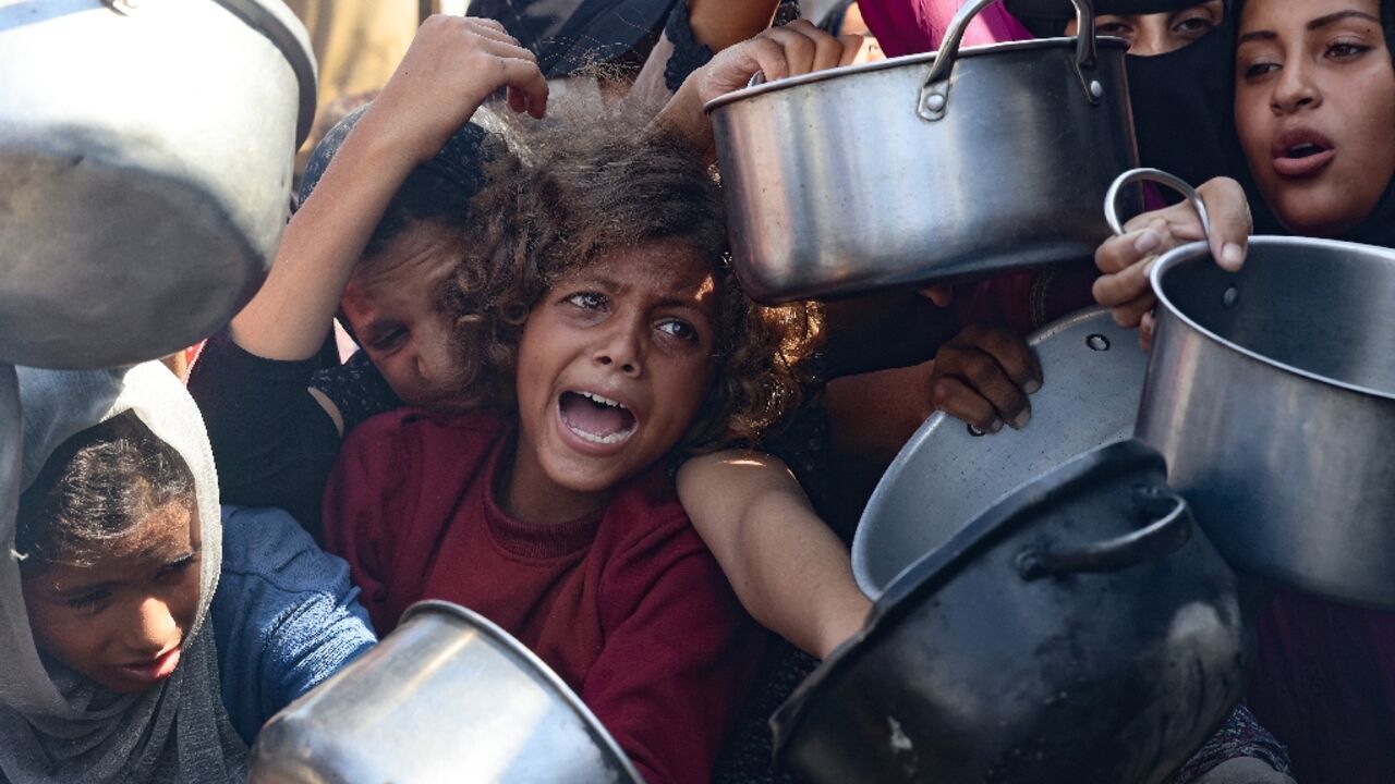 Palestinian women and children hold out their empty pots in front of a charity kitchen in Khan Yunis in the southern Gaza Strip on August 21, 2025