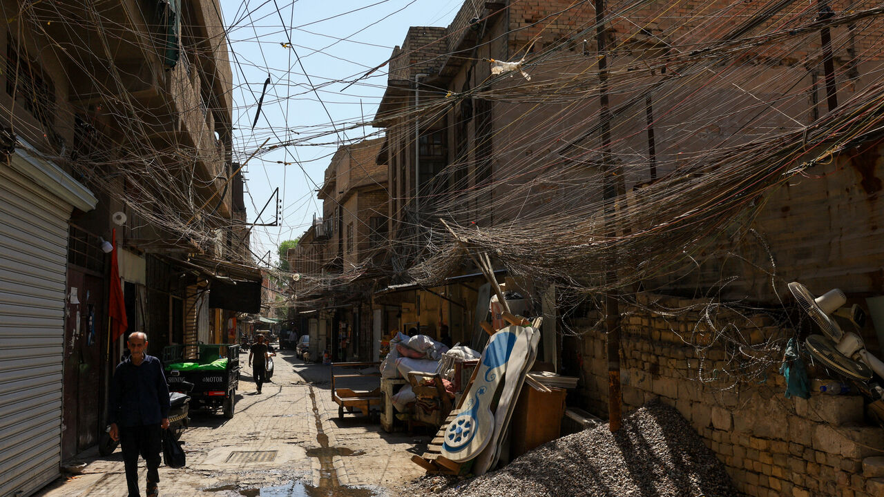People walk along an old street as a tangled web of electrical wires from a generator supplying homes with electricity hangs above buildings, in Baghdad, Iraq, September 10, 2025. REUTERS/Thaier Al-Sudani