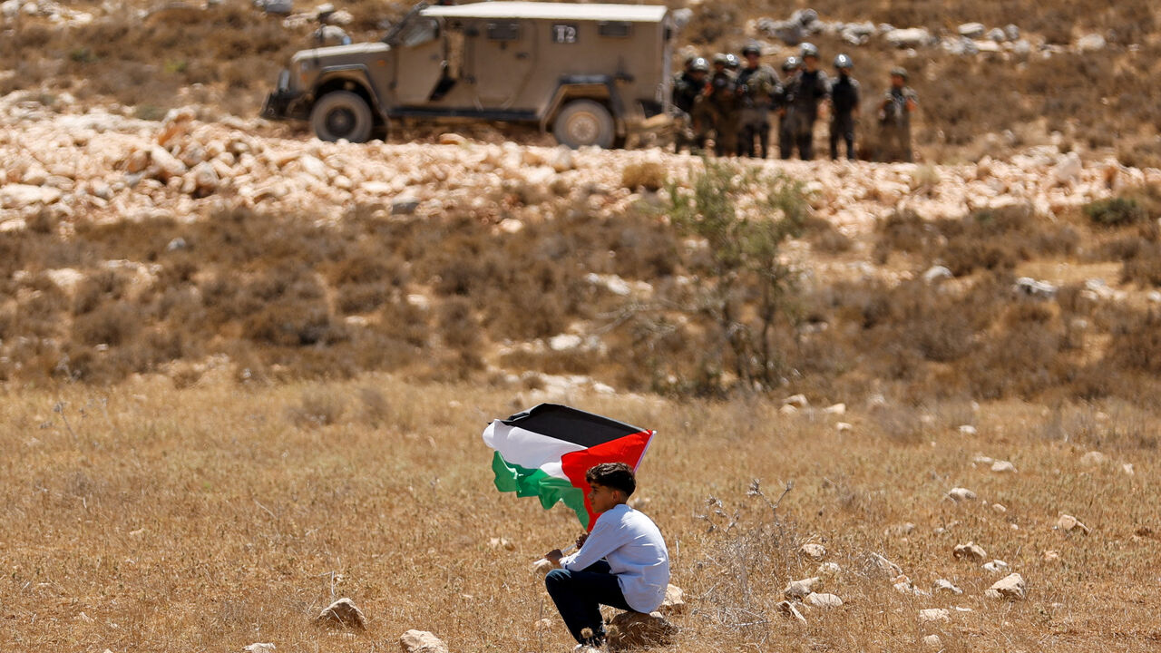 A boy holds a Palestinian flag during a demonstration against what Palestinians say is Israel's confiscation of their land, as Isareli security forces stand guard, in Raba, near Jenin, in the Israeli-occupied West Bank July 18, 2025. REUTERS/Raneen Sawafta/File Photo