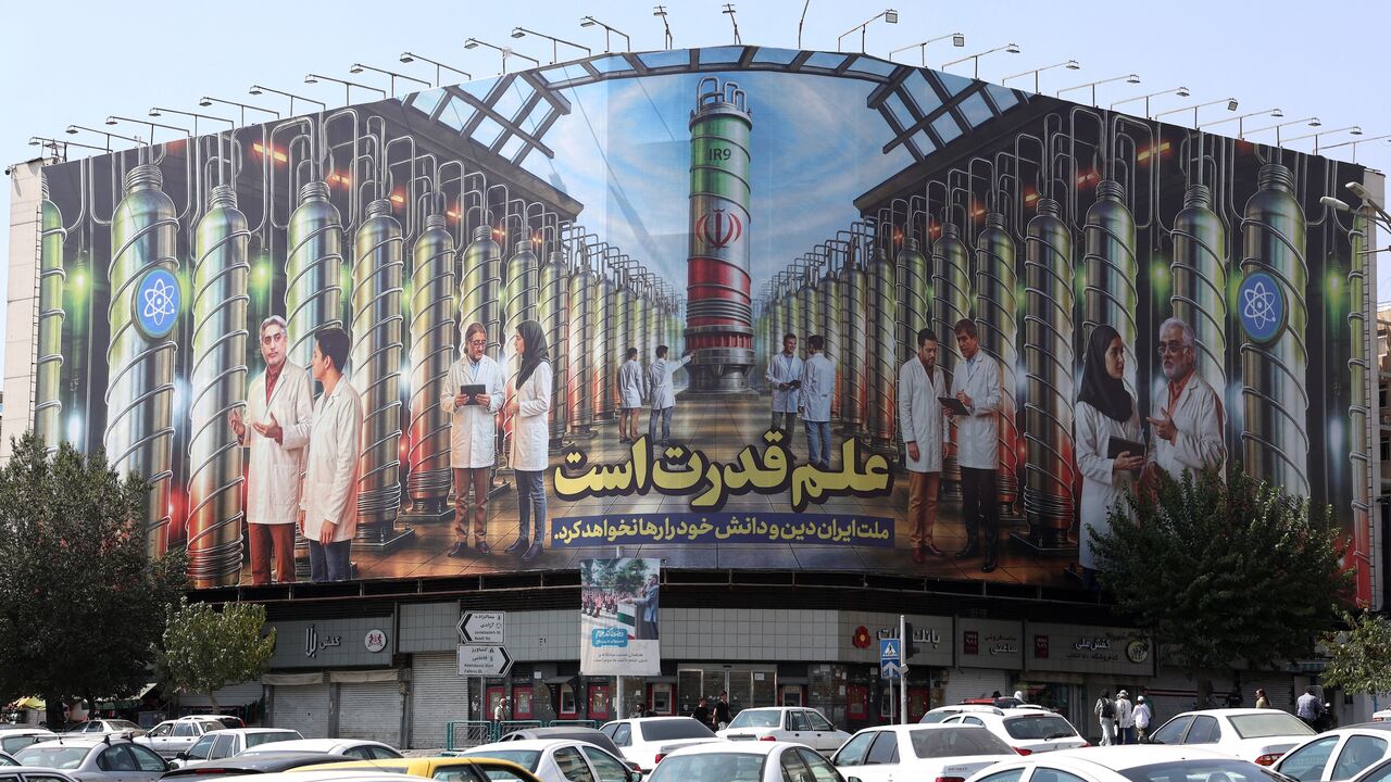 Iranians drive next to a billboard displaying pictures of nuclear scientists, centrifuges and a sentence reading in Farsi, "Science is the power," at the Enqelab Square in Tehran, on Aug. 29, 2025.