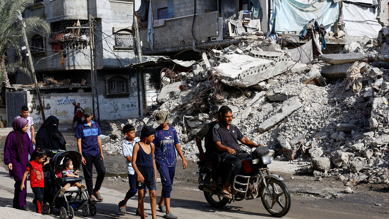 Palestinians walk past a residential building destroyed in previous Israeli strikes, after Hamas agreed to release hostages and accept some other terms in a U.S. plan to end the war, in Nuseirat, central Gaza Strip October 4, 2025. REUTERS/Mahmoud Issa