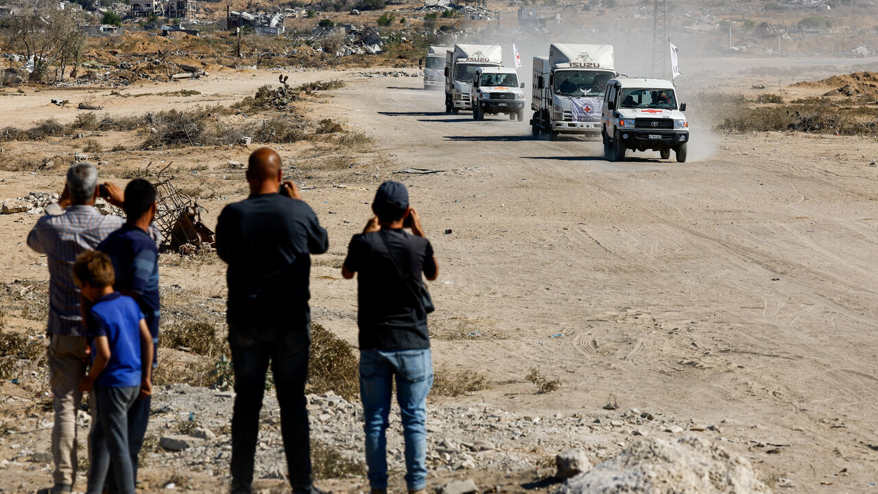 People look at Red Cross vehicles as they escort trucks transporting the bodies of deceased Palestinians held by Israel during the war, after their release, amid a ceasefire between Israel and Hamas, in Khan Younis, southern Gaza Strip, October 15, 2025. REUTERS/Mahmoud Issa