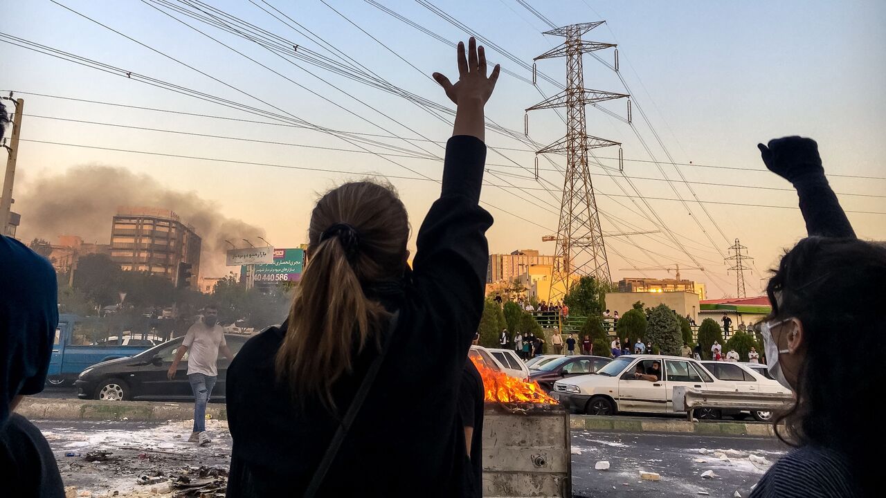 Iranian women without wearing hijab shout slogans while gathering around a burning dumpster during a protest near Punak square, on Oct. 1, 2022