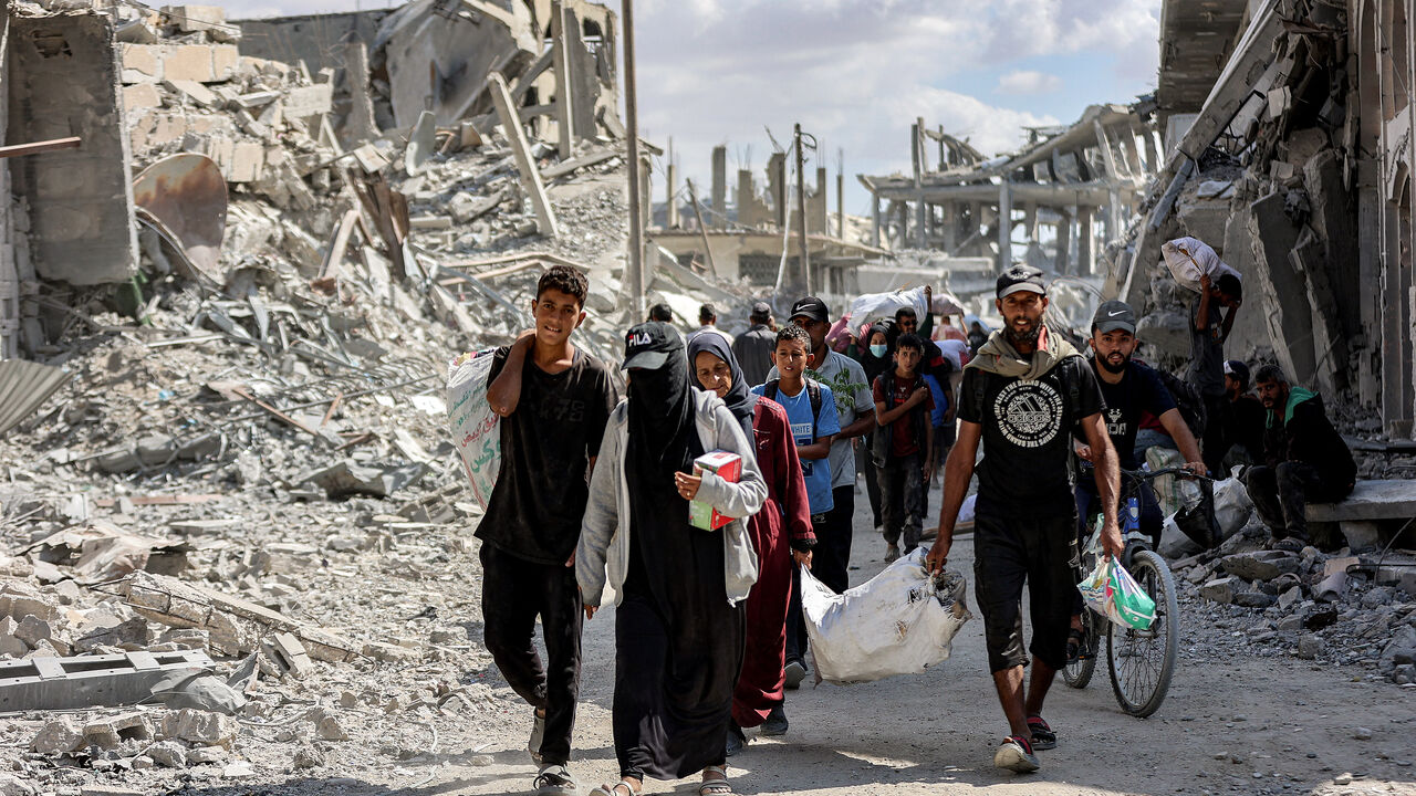 People walk along a destroyed road past heavily-damaged buildings in the centre of Khan Yunis in the southern Gaza Strip on Oct. 10, 2025, as the displaced return to their homes after Israeli forces' withdrawal.