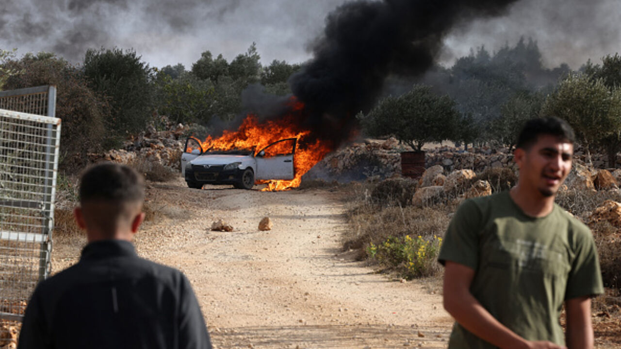 TOPSHOT - Palestinians stand near a burning car reportedly set alight by Israeli settlers attempting to disrupt them harvesting olives near the occupied West Bank village of Turmos Ayya near Ramallah on October 19, 2025. (Photo by HAZEM BADER / AFP) (Photo by HAZEM BADER/AFP via Getty Images)