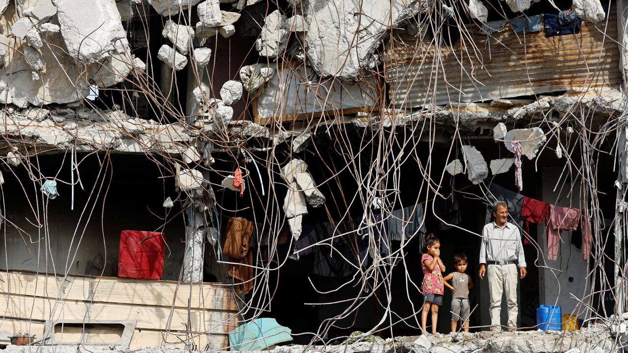 A Palestinian man and children stand at a heavily damaged building surrounded by rebar and rubble, amid a ceasefire between Israel and Hamas, in Gaza City, November 2, 2025. REUTERS/Mahmoud Issa