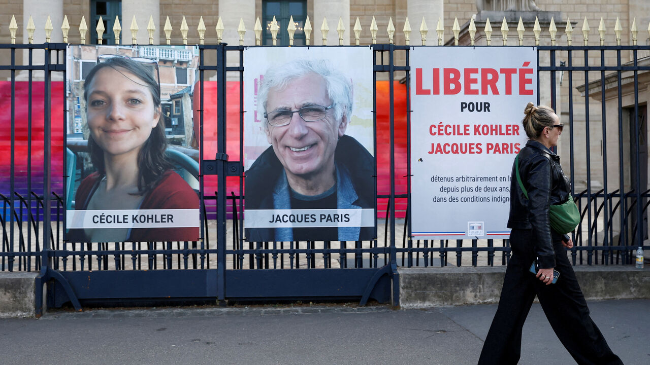 FILE PHOTO: A woman walks past posters with the portraits of Cecile Kohler and Jacques Paris, two French citizens held in Iran, in Paris, France, May 7, 2025. The slogan reads "Freedom for Cecile Kohler and Jacques Paris". REUTERS/Abdul Saboor/File Photo