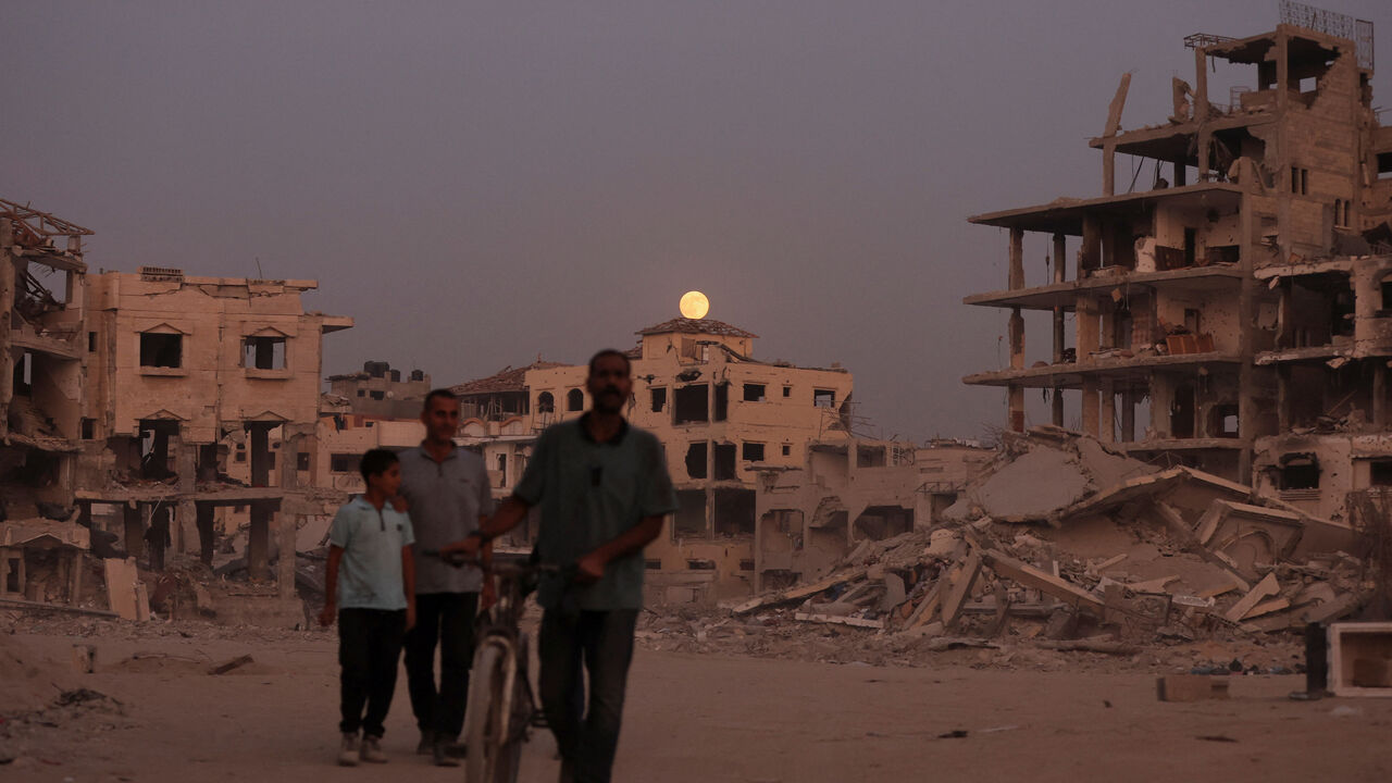 The Beaver Moon supermoon rises above destroyed buildings as Palestinians walk past the rubble amid a ceasefire between Israel and Hamas, in Gaza City, November 5, 2025. REUTERS/Dawoud Abu Alkas