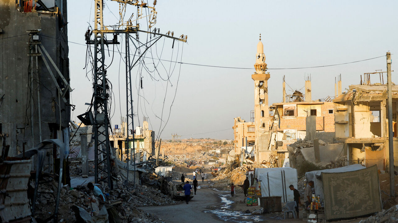 People walk past damaged electricity poles in Nuseirat, central Gaza Strip, October 31, 2025. REUTERS/Mahmoud Issa