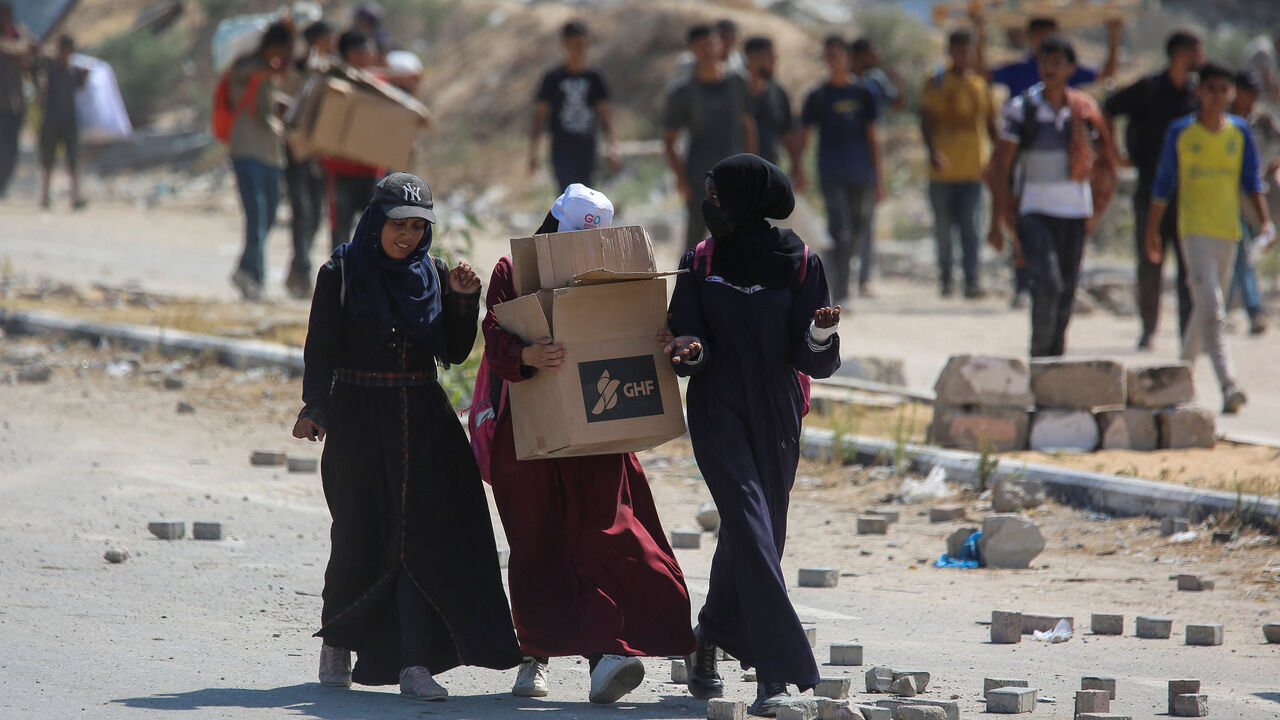 A Palestinian woman carries a box as people seek aid supplies from the U.S.-backed Gaza Humanitarian Foundation (GHF), in the central Gaza Strip, August 4, 2025. REUTERS/Stringer