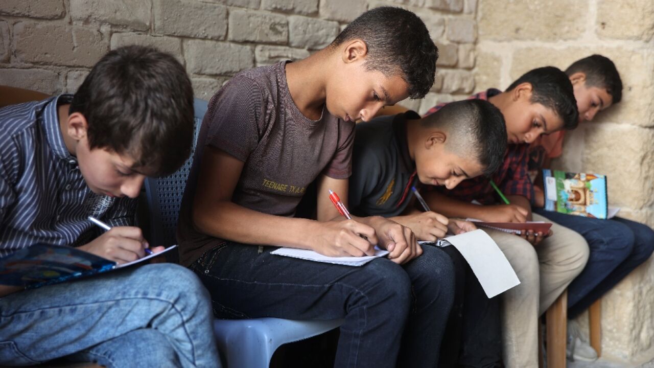 Palestinian children take notes as they attend a class in the historic Al-Kamaliya al-Othmanya school in Gaza City's Old Town, as part of a volunteer initiative organised by displaced teachers, in Gaza City