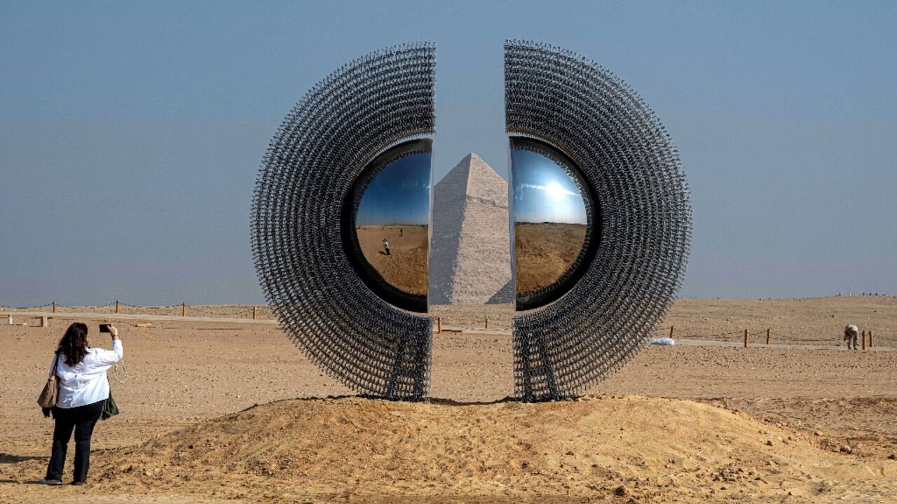 A woman takes a picture of the art installation "The Shen" by artist by Mert Ege Kose during the fifth edition of the "Forever is Now" art exhibition by Art d’Egypte at the Giza pyramids necropolis