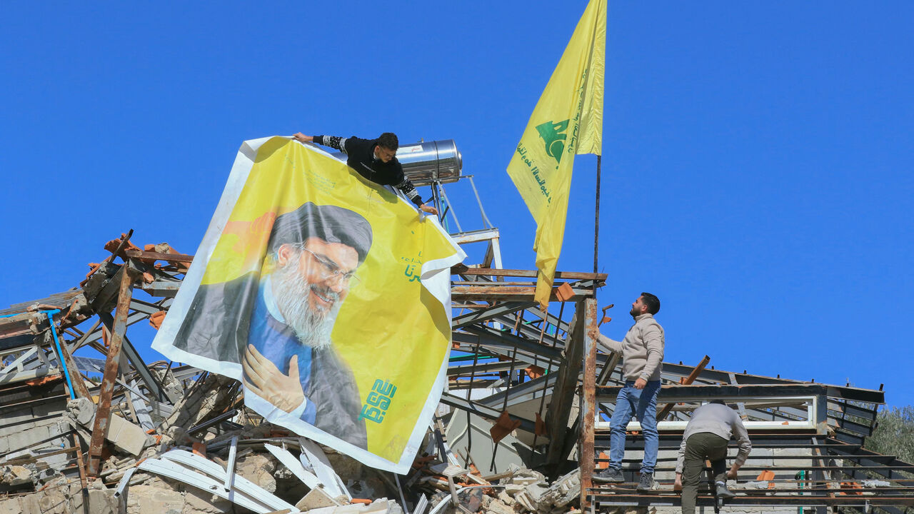 Residents hang a poster bearing a portrait of Hezbollah's slain leader Hassan Nasrallah and the flag of the Iran-baked party on the rubble of a destroyed house in the southern border village of Adaisseh, following the Israeli army's withdrawal on Feb. 18, 2025. 