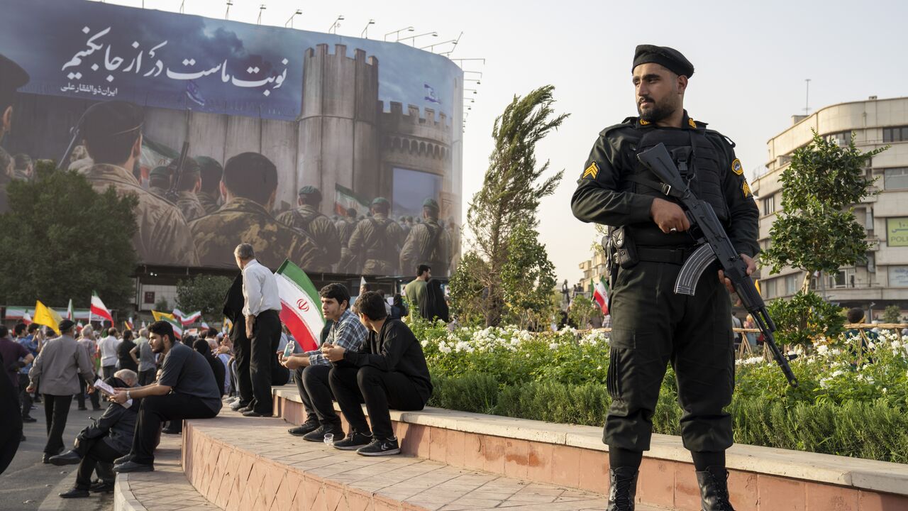 TEHRAN, IRAN - JUNE 24: A Police officer stands guard as demonstrators wave flags and cheer during a gathering to honor Iran’s military forces, following the announcement of a ceasefire between Israel and Iran, on June 24, 2025 in Tehran, Iran. Iranian authorities announced this morning they would agree to a ceasefire with Israel, whose attacks on Iran's military and nuclear sites on June 13 sparked a daily exchange of missiles between the countries. (Photo by Majid Saeedi/Getty Images)