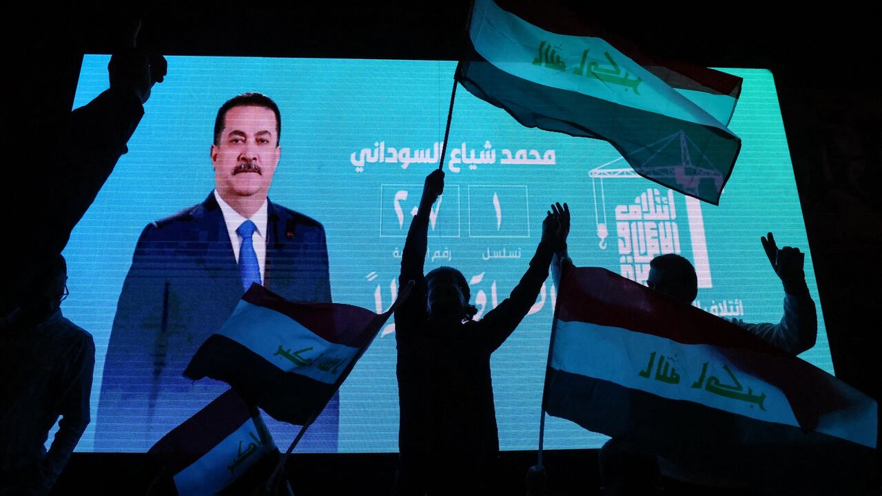 Supporters of incumbent Iraqi Prime Minister Mohammed Shia al-Sudani wave national flags in front of a screen displaying his portrait as they celebrate following the announcement of preliminary election results in Baghdad on Nov. 12, 2025.
