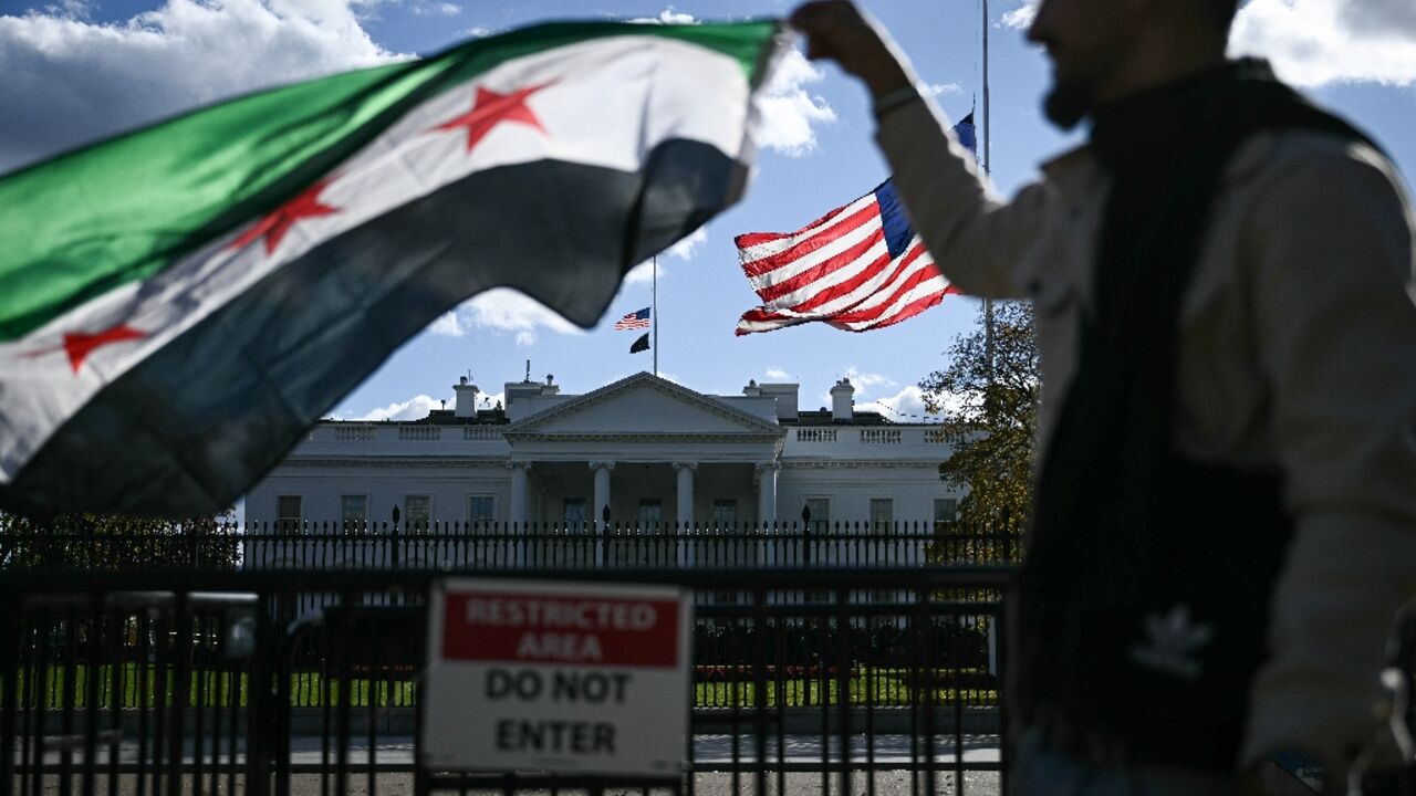 A man holds a Syrian flag across the street from the White House after Syrian President Ahmed al-Sharaa's meeting with US President Donald Trump 