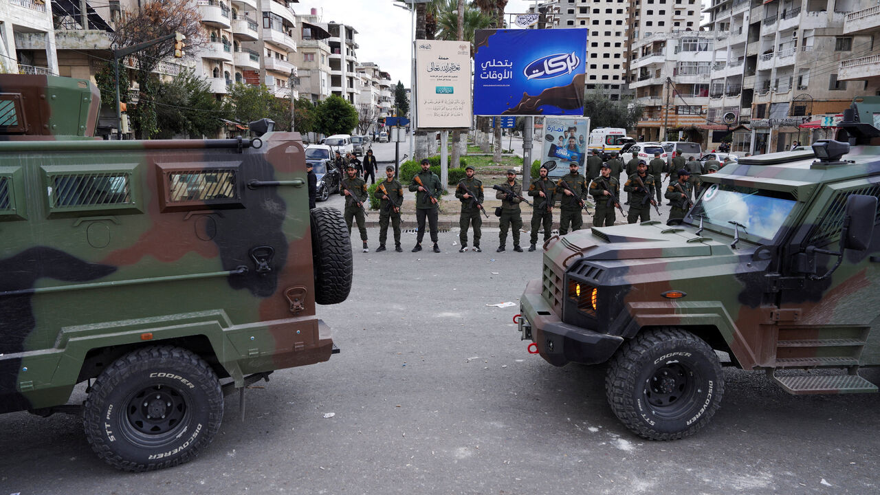 FILE PHOTO: Members of the Syrian Security forces stand guard near military vehicles on the day people from the Alawite sect protest as they demand federalism and an end to what they say is the killing and violations against Alawites, in Latakia, Syria, December 28, 2025. REUTERS/Karam al-Masri/File Photo