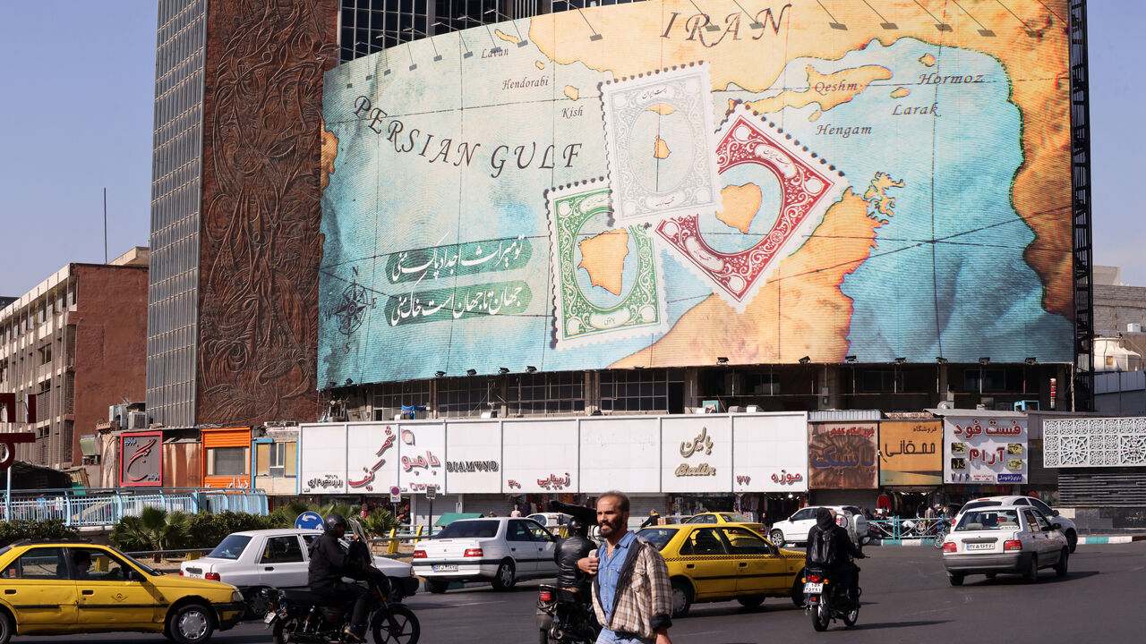 People walk and drive past a billboard covering the facade of a building on Vali-Asr square, depicting as postage stamps the disputed Abu Musa and Greater and Lesser Tunb islands that were seized by Iran in 1971, in Tehran on October 26, 2024. Residents of Tehran awoke and went about their business as planned on October 26 after their sleep was troubled by Israeli strikes that triggered blasts that echoed across the city. (Photo by ATTA KENARE / AFP) (Photo by ATTA KENARE/AFP via Getty Images)