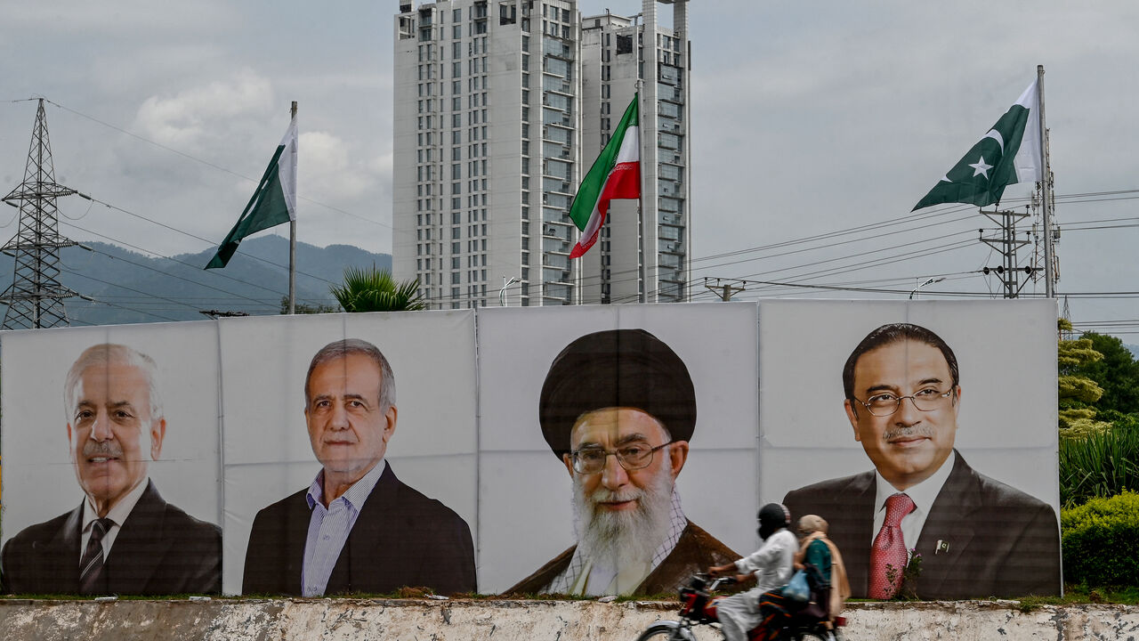 A motorcyclist rides past a banner with the portraits of (L-R) Pakistan's Prime Minister Shehbaz Sharif, Iran's President Masoud Pezeshkian, Iran's Supreme Leader Ayatollah Ali Khamenei and Pakistan's President Asif Ali Zardari, welcoming Iran's president during his state visit in Islamabad on August 2, 2025. (Photo by Farooq NAEEM / AFP) (Photo by FAROOQ NAEEM/AFP via Getty Images)
