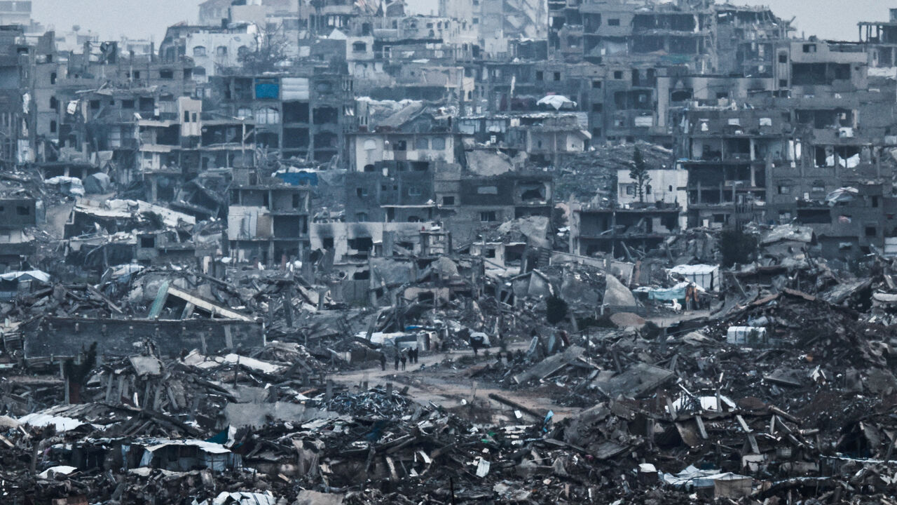 Palestinians walk near damaged buildings in the Gaza Strip, as seen from Israel, December 29, 2025. REUTERS/Amir Cohen