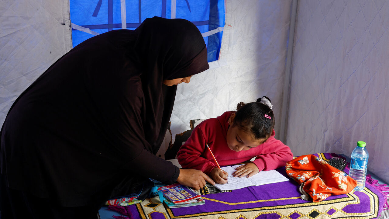 Displaced Palestinian mother, Yasmine Al-Aajouri, helps her seven-year-old daughter Toulin Al-Hindi with her homework inside their tent near the Israeli-designated "yellow line", in Beit Lahiya, northern Gaza Strip, January 6, 2026. REUTERS/Mahmoud Issa